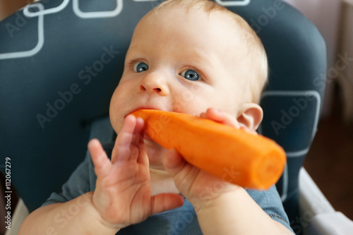 Baby eating carrot in a chair