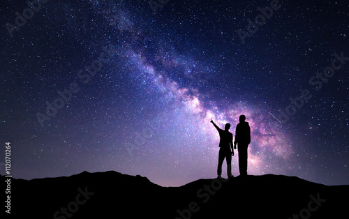 Milky Way with silhouette of a family on the mountain. Father and a son who pointing finger in night starry sky. Night landscape. Beautiful Universe. Space. Travel background with sky full of stars