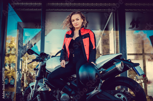 Blond female posing near motorcycle.