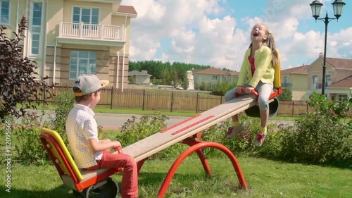Little boy and girl enjoying riding seesaw on green lawn in slow motion photo