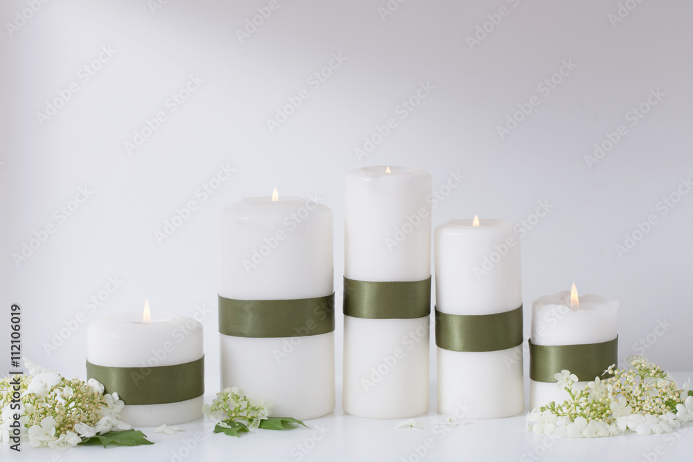 white candles burning with flowers on a white shelf white candles burning with flowers on a white shelf