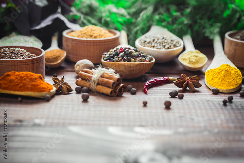 Fotografie Beautiful colorful spices in wooden spoons and bowls with lettuce, dill and Basil on an old wooden brown table
