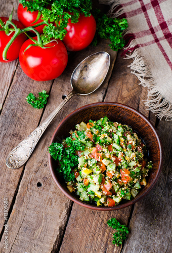 Fresh tabbouleh, a Middle Eastern salad, in clay bowl on wooden background. Selective focus. Toned image