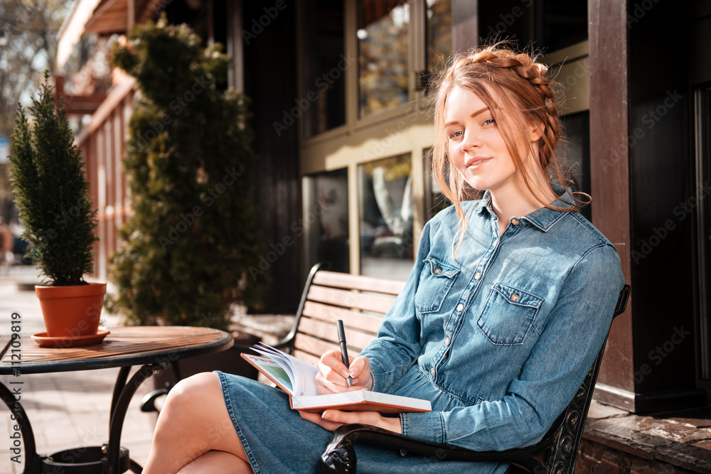 Fototapeta premium Pensive woman writing in notebook sitting in outdoor cafe