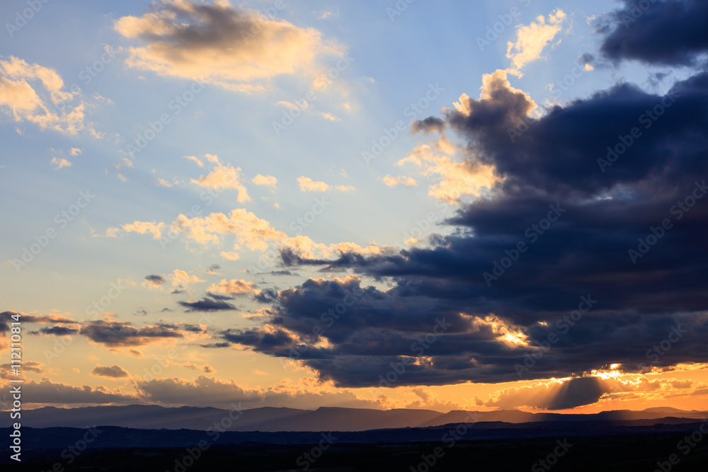 Obraz premium Sun shining through dark clouds in evening