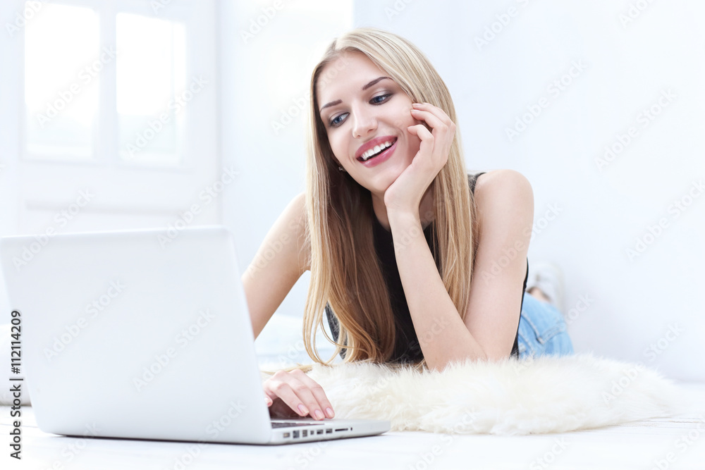 Happy young woman lying on the floor at home and using laptop Happy young woman lying on the floor at home and using laptop