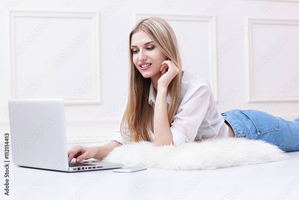 Happy young woman lying on the floor at home and using laptop Happy young woman lying on the floor at home and using laptop