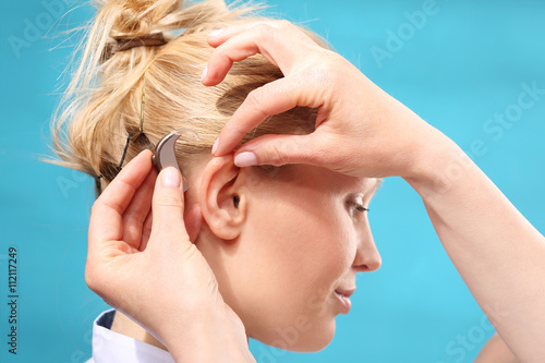 Zakładanie aparatu słuchowego. Lekarz zakłada kobiecie aparat słuchowy na ucho 