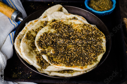 Freshly baked flatbread with mixed spice and herbs - zaatar or zatar on vintage wooden background. Selective focus. Toned image