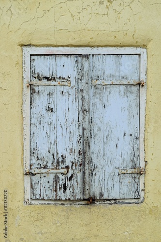 Altes Holzfenster mit geschlossenen Schlagläden in einem verfallenen, sanierungsbedürftigen Haus © ArndtLow