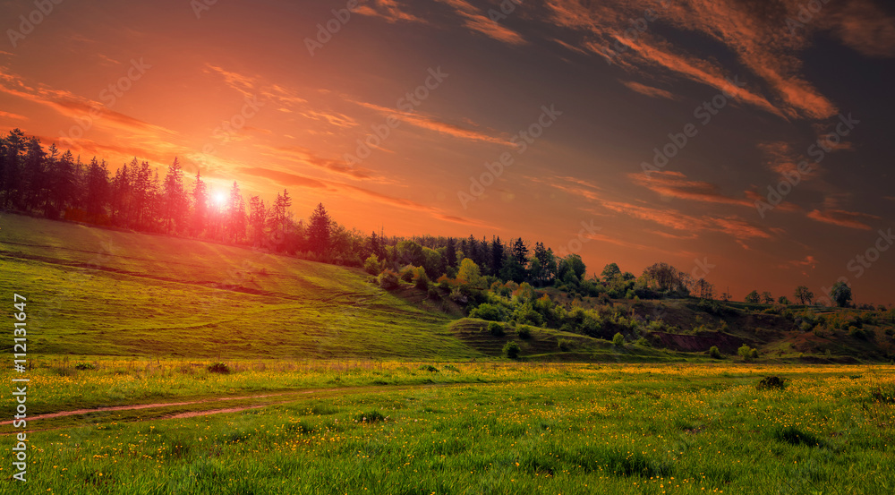 Rural landscape with a hill. Green meadow under sunset, colorful sky with clouds Dramatic morning scene. Beautiful natural landscape