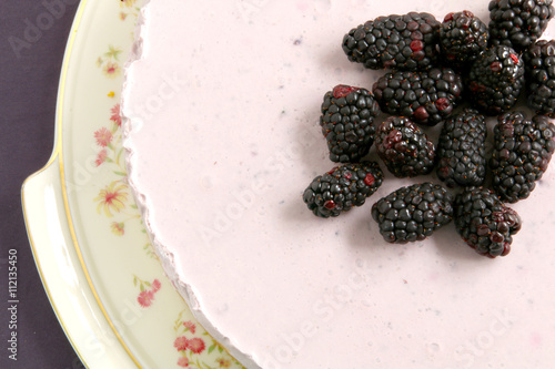 Part of a violet cheesecake with some fresh blacberries on the top on a caramic plate. photo