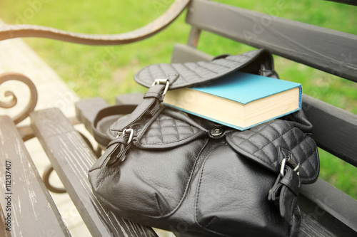 Leather backpack with book on bench outdoors