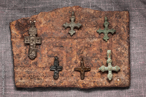 five copper and one iron Christian early medieval crosses lie on a rusty plate photo