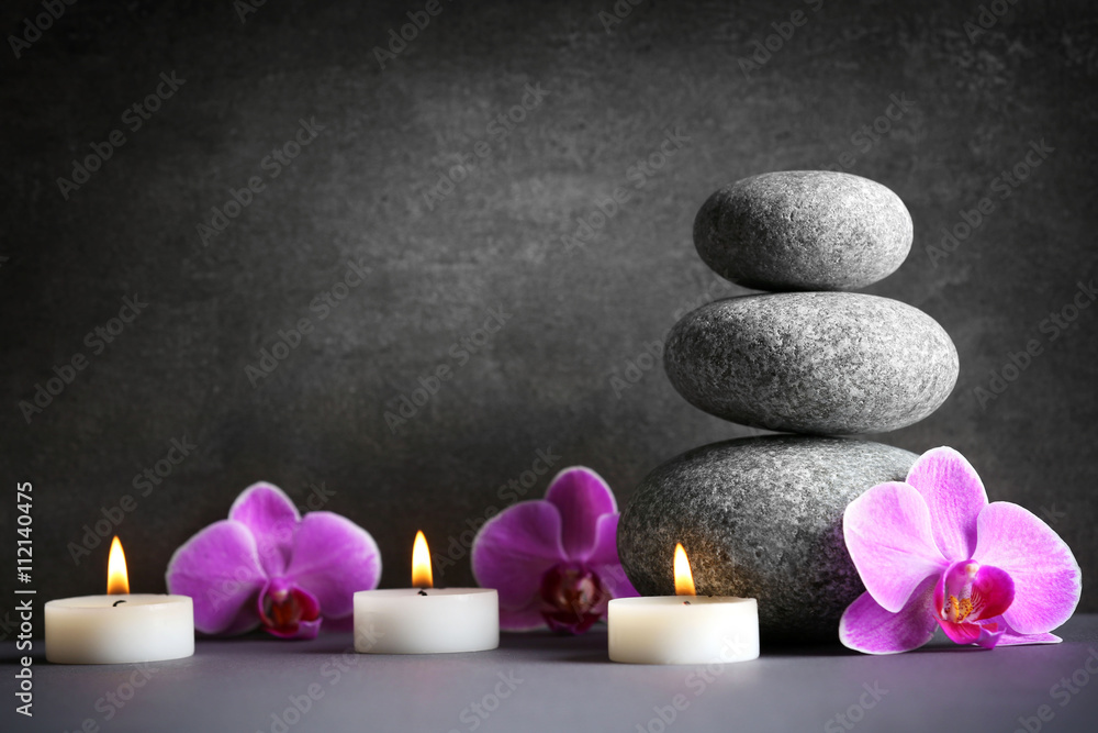 Composition of spa pebbles, flowers and candles on grey background