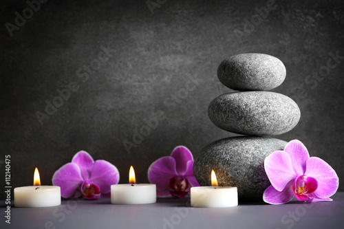 Composition of spa pebbles  flowers and candles on grey background