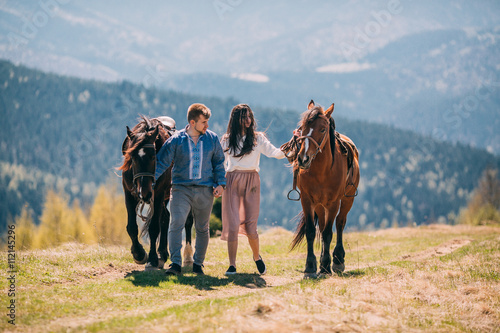 Young couple walking with two horses in the mountains