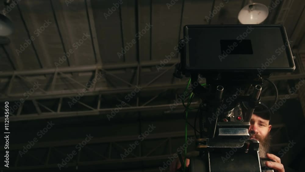 Low shot of camera operator panning professional camera in dark studio
