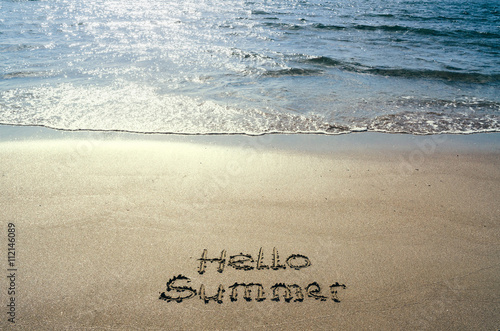 Hello summer handwritten on beach sand. Water sea background.
