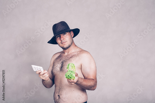Naked corpulent man holding pharmaceuticals and vegetable