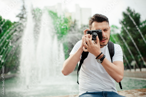 Outdoor summer lifestyle portrait of a handsome man having fun in city with camera. Travel photo of photographer. Young man taking photo.
