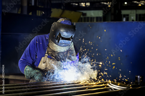 Worker dressed in protective uniform welding metal frame