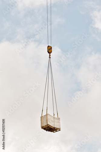 heavy load of bricks hanging on the hook of a crane, blue cloudy sky background