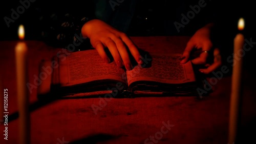 A female witch considers an old book on a table with burning candles. Shooting with the shallow depth of field