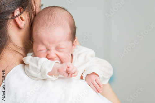 Newborn baby screaming in pain with colic on mother's shoulders photo