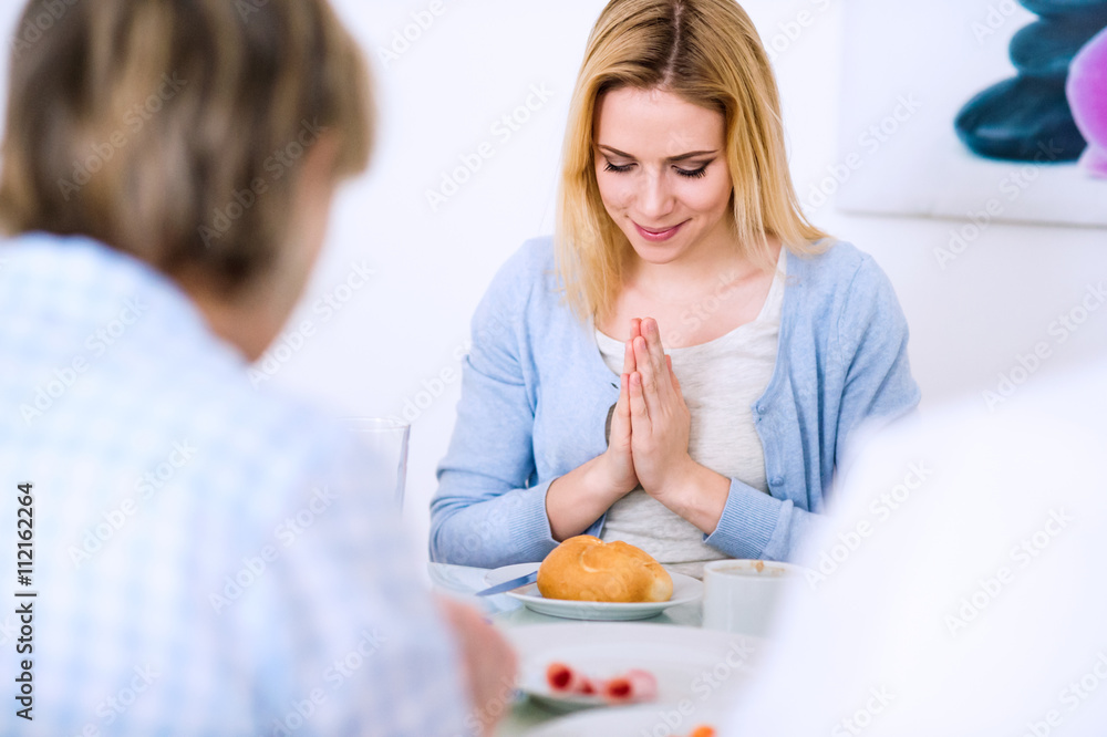 Young woman praying before having meal with her family. Young woman praying before having meal with her family.