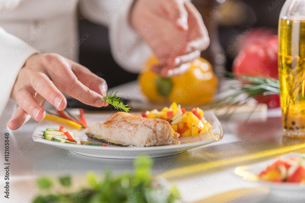 Hands of a chef putting the finishing touches on his fish dish