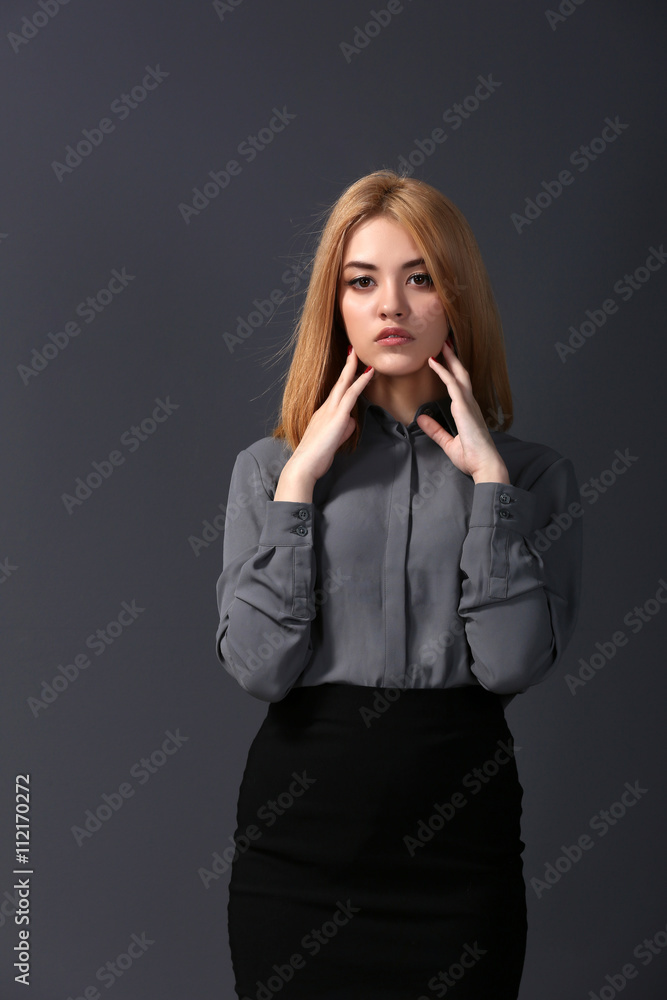 Beautiful blonde young woman in grey shirt and black skirt on dark grey wall background Beautiful blonde young woman in grey shirt and black skirt on dark grey wall background