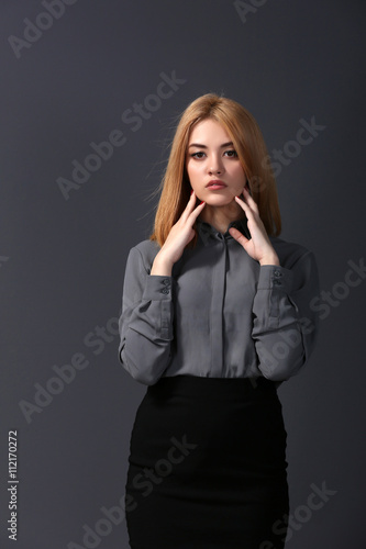 Beautiful blonde young woman in grey shirt and black skirt on dark grey wall background