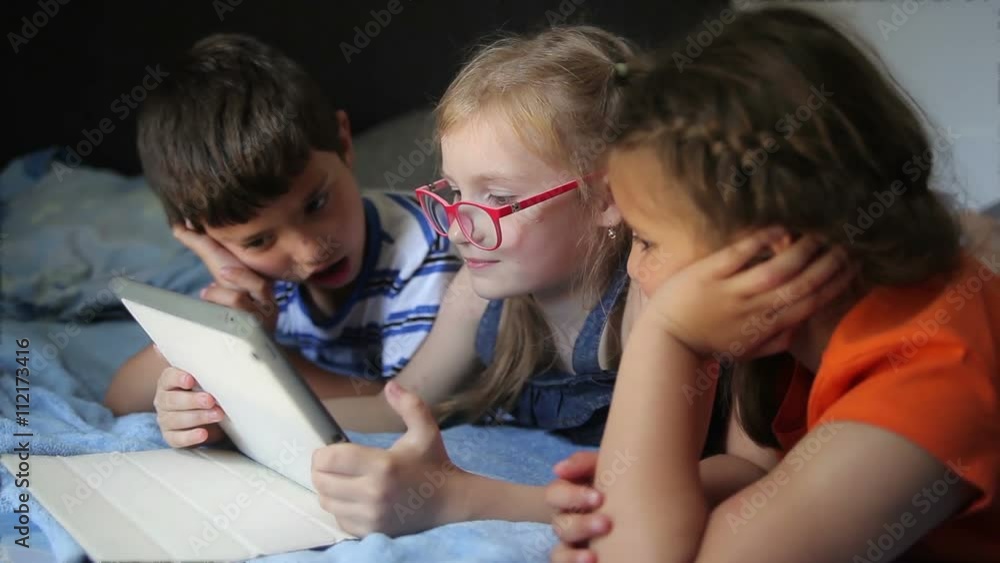 Children play on the tablet while lying on the bed Children play on the tablet while lying on the bed