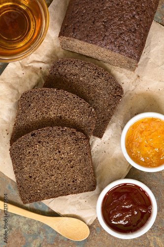 Slices of pumpernickel dark rye bread with strawberry and orange jam, cup of tea on the side, photographed overhead with natural light