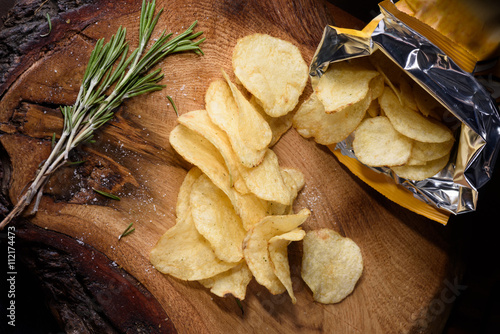 Fotografie Heap of potato chips with rosemary over wooden background