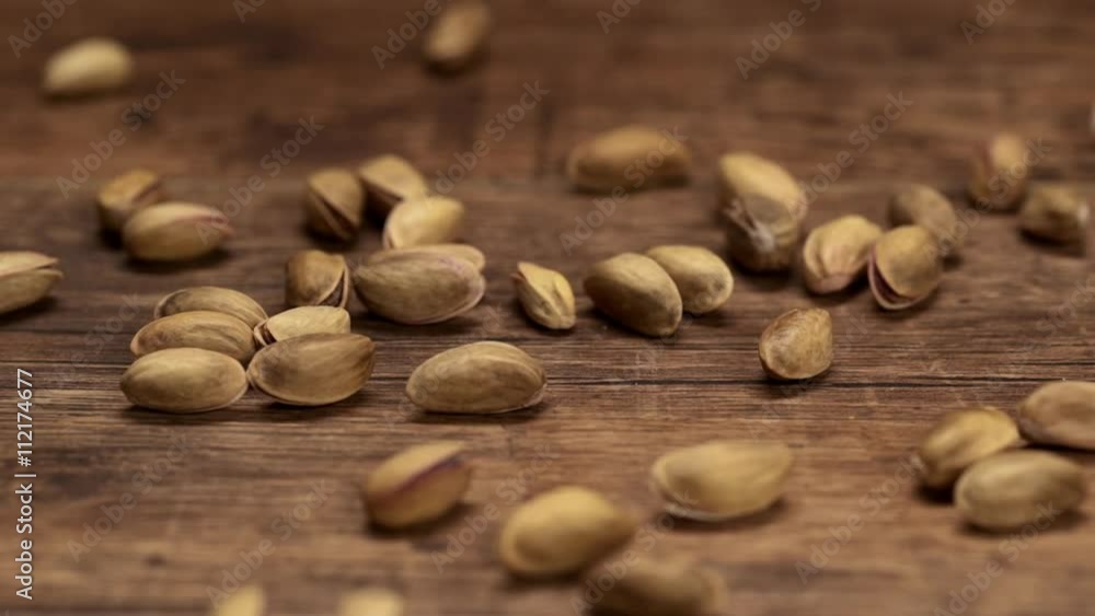 Pistachio nuts falling down on wooden table. Close up. Slow motion