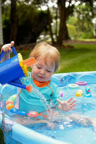 toddler boy playing with watering can in baby pool