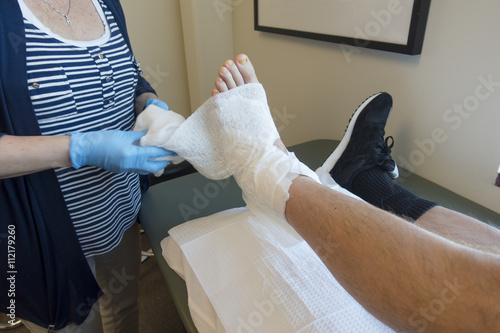 Podiatrist, Doctor or Physical Therapist Wrapping Foot Cast of Patient with Broken, Fractured or Sprained Ankle photo