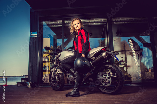 Blond female posing near motorcycle.