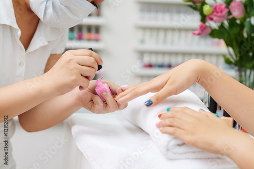 Manicurist applying pink nail polish, side view