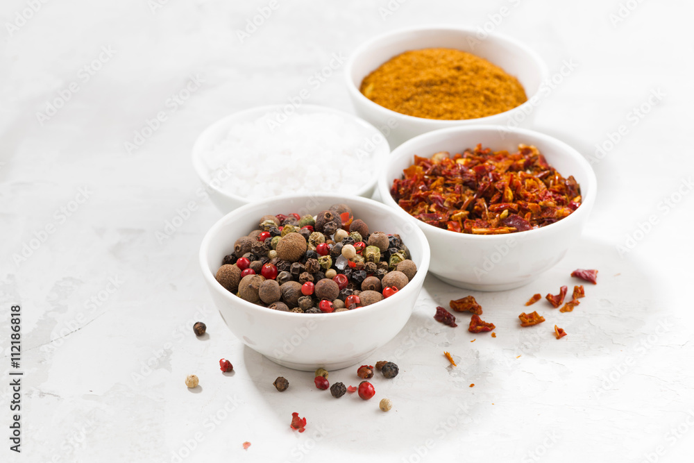 assortment of pepper, salt and spices in bowls on white table assortment of pepper, salt and spices in bowls on white table