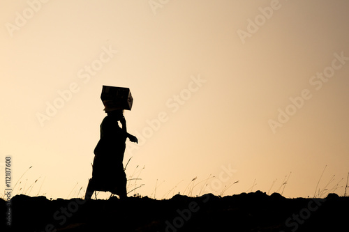 silhouette woman carrying belonging on head call walking in the wonderful orange sunset