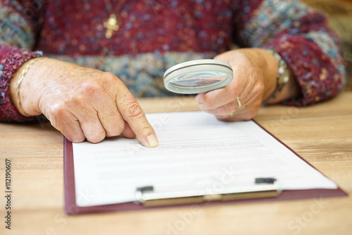 elderly person with magnifying glass checking document
