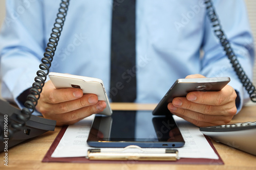 busy businessman in office at the desk using two mobile phones, photo