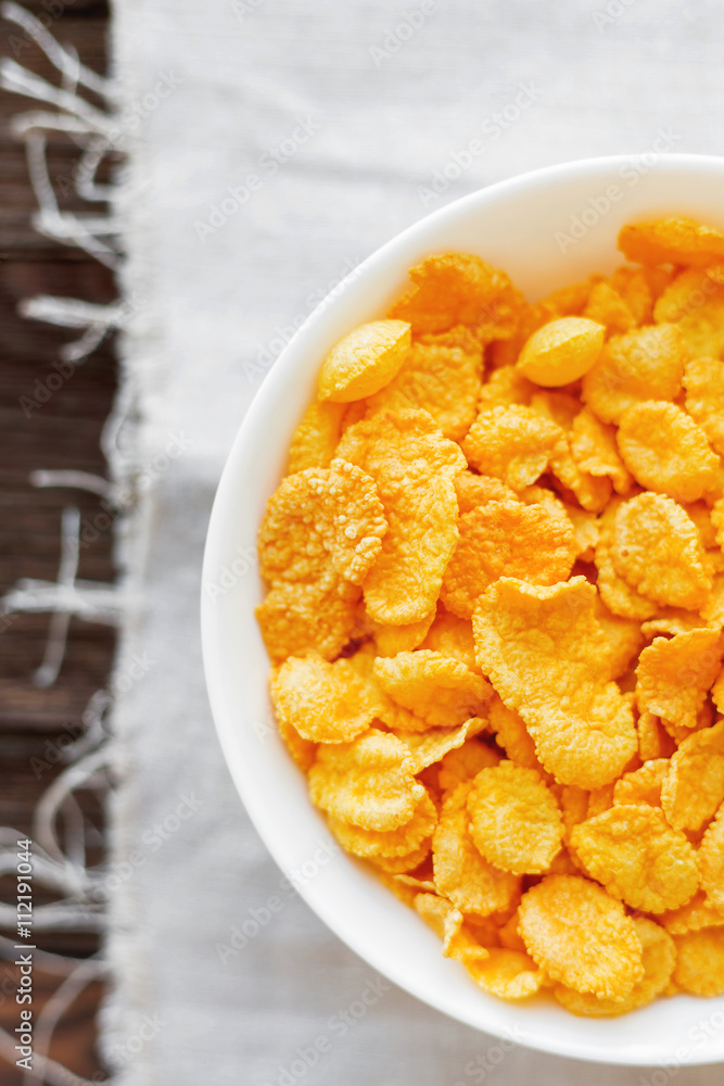 Tasty corn flakes in bowl. Rustic wooden background with homespun napkin. Healthy crispy breakfast snack. Top view, flat lay. Tasty corn flakes in bowl. Rustic wooden background with homespun napkin. Healthy crispy breakfast snack. Top view, flat lay.