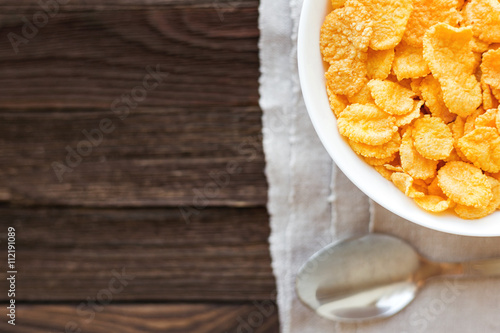 Tasty corn flakes in bowl. Rustic wooden background with homespun napkin. Healthy crispy breakfast snack. Place for text. Top view, flat lay.