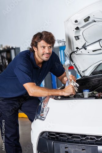 Thoughtful Mechanic Leaning On Car With Open Hood
