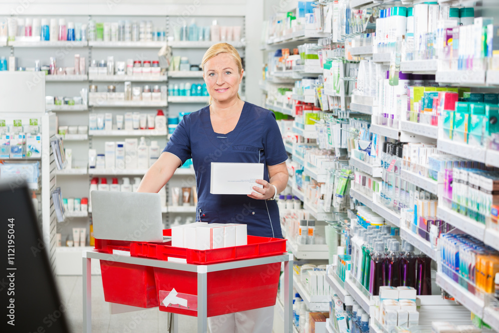 Fototapeta premium Smiling Pharmacist Updating Stock In Laptop At Pharmacy