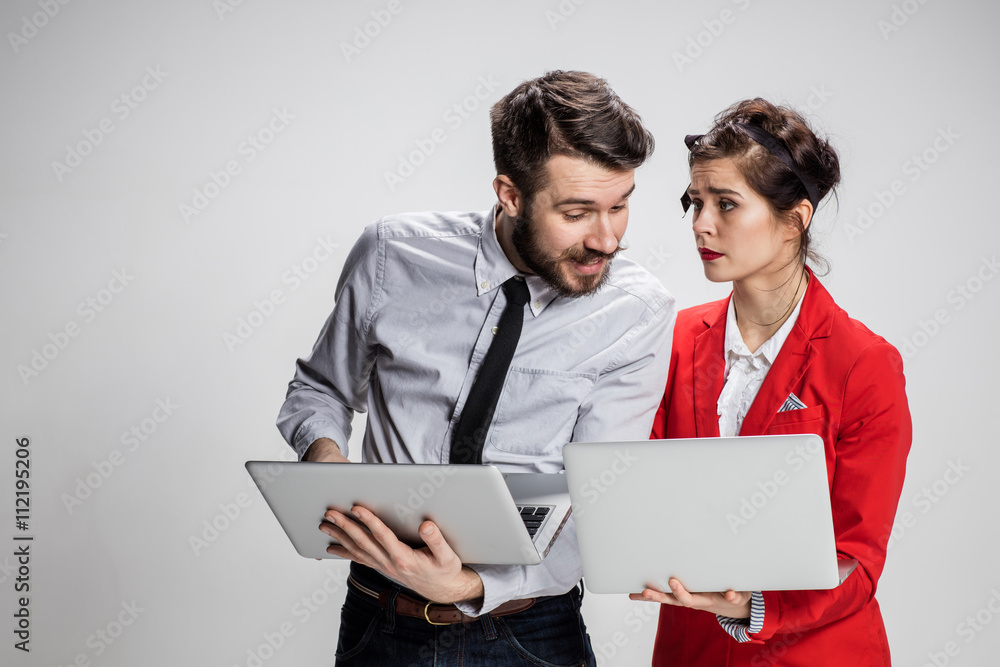 The young businessman and businesswoman with laptops communicating on gray background The young businessman and businesswoman with laptops communicating on gray background